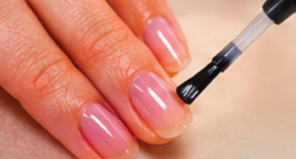 A nail polish brush applying a thin coat of clear base coat to a fingernail